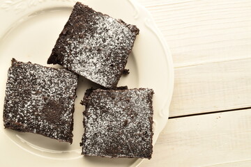 One chocolate sweet brownie with cherries with a spoon from a tree, close-up, on a wooden table.