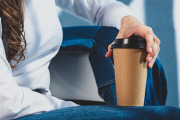 Naklejka premium Young woman in white t shirt and denim jeans holds disposable coffee cup. Youth, modern lifestyle. Coffee break, cosy relaxing moment. 