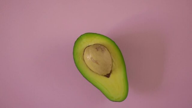 Avocado on a pink background. Half a rotating avocado on a isolated colored background. Looping food video 