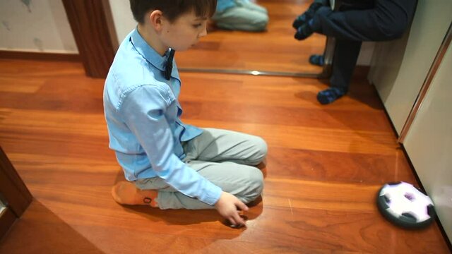 Bored child sitting on the floor plays with a toy. Knocks against the wall, catches with his hands. Leisure activities in self-isolation at home. In the background a mirror.