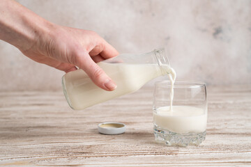 Pouring fresh milk from glass bottle to glass. Hand holding a bottle with milk on wooden table