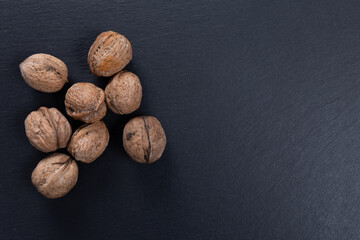 raw walnuts. nuts with shell photographed on top of a black plate