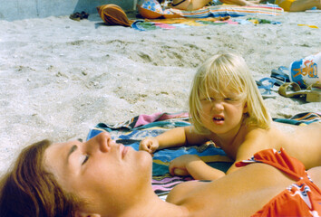 1976 vintage, seventies, retro colourful image of young girl looking up from her beach towel and a...