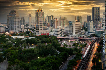 Bangkok business district with the public park area anf the sky train in the foreground at sunset time.