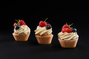 Three vanilla cupcakes with berries and cream.