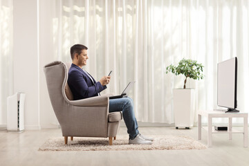 Man in an armchair with a laptop computer and a mobile phone