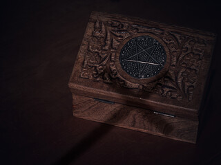 A wooden box with a pentagram on the lid and the shadow over a cross over it