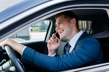 Smiling businessman talking on smartphone while driving car on blurred foreground.