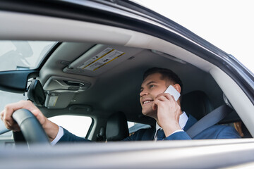 Cheerful businessman talking on smartphone while driving car on blurred foreground.