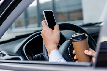 partial view of man holding coffee to go and chatting on smartphone in car on blurred foreground.