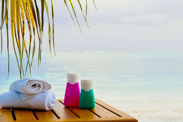 Sun cream bottles with white rolled towels on the sea shore view. Beach accessories outdoors