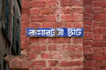 Picture of red brick wall. Translation on name plate text "Kumartuli Street".
