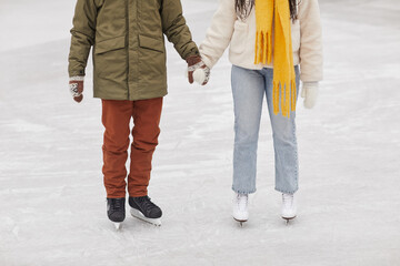 Close-up of couple in warm clothing standing on skating rink and holding hands