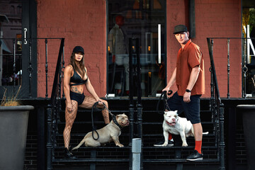 young stylishly dressed man and woman with an athletic figure with two american bully dogs on city...