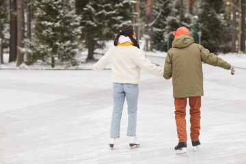 Rear view of couple in warm clothing skating together on skating rink in winter