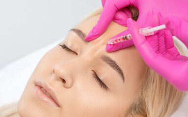 Cosmetologist makes rejuvenating anti wrinkle injections on the face of a beautiful woman. Female...