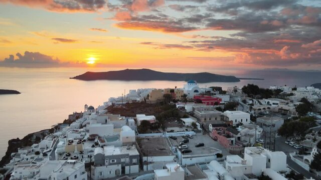 Aerial establishing shot flying over Thera town in Santorini and the sun setting on background