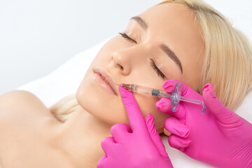Cosmetologist does injections for lips augmentation and anti wrinkle in the nasolabial folds of a...