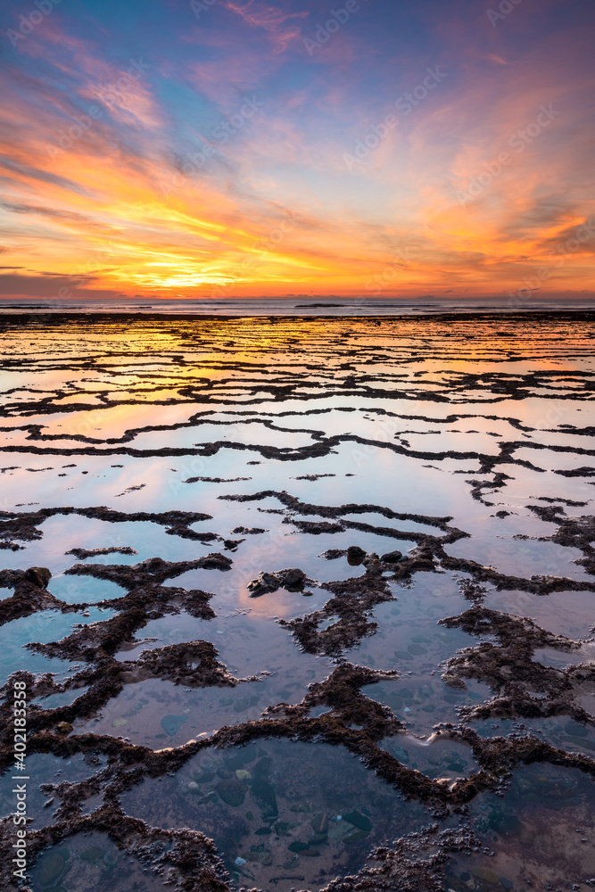 Sticker vertical view of a beautiful sunset over the ocean with rocky beach and tidal pools in the foregroun