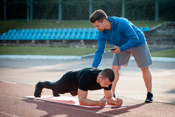 man doing plank exercise and workout with personal fitness trainer outdoor