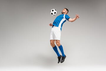 Naklejka na ściany i meble Sportsman training with football while jumping on grey background