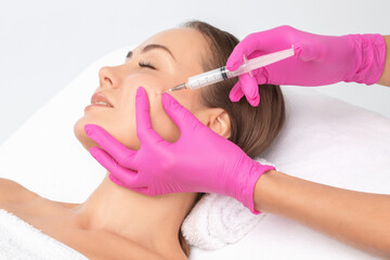 Fototapeta premium Cosmetologist makes lipolytic injections to burn fat on the chin, cheeks and neck of a woman against double chin. Female aesthetic cosmetology in a beauty salon.Cosmetology concept.