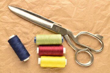 Several spools of colored thread with metal scissors, close-up, on brown paper.