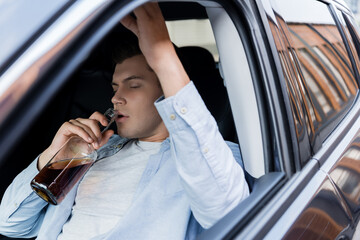 drunk, sleepy man sitting in car and drinking whiskey with closed eyes.