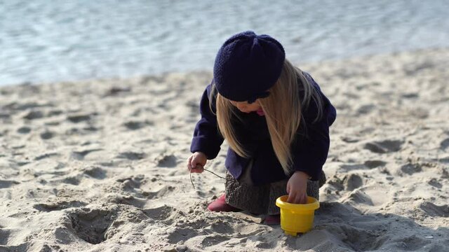Cute little girl playing with white sand outdoor on sandy beach in cold season