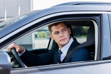 Businessman looking at window while driving auto on blurred foreground.