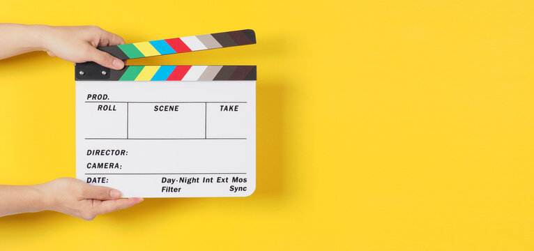Hand is holding clapper board or movie slate or film slate.It is used in video production and cinema ,movies industry on yellow background