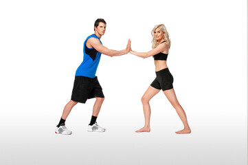 Portrait of a fit, young, white coach in a blue shirt & female athlete with curly long blond hair posing together touching palms in a studio with a white background wearing black shorts & sports bra.
