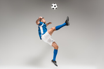 Sportsman in knee socks and sportswear jumping while playing soccer on grey background