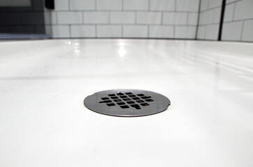 Close up of a clean shower drain in a modern, white hotel bathroom