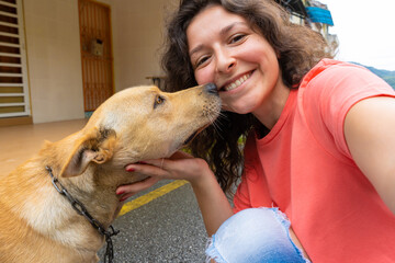 A beautiful brunette girl makes a selfie with her beloved dog. The dog is very happy and excited kisses the girl. Pets and their owners