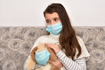 Young girl sitting on the sofa and holding her dog toy wearing medical protective face masks