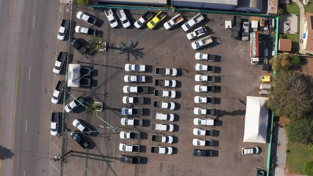 Aerial bird's eye descending spiral shot of trucks lined up at a used automotive dealership lot. 4K