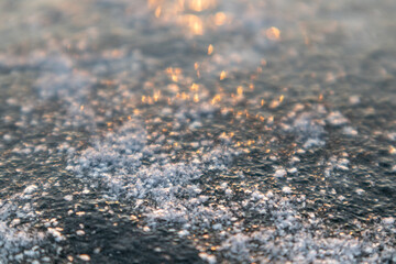 Frozen ice cold deep lake surface covered with snow close-up sparkling in orange sunset light. Blurred background