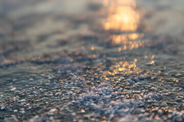 Frozen ice cold deep lake surface covered with snow close-up sparkling in orange sunset light. Blurred background