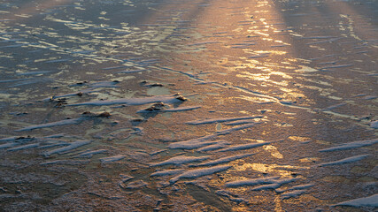 Frozen ice cold deep lake surface covered with snow close-up sparkling in warm orange sunset light background