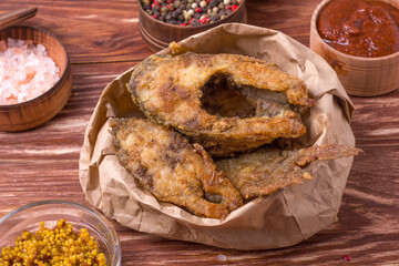 Pieces of fried carp in a paper bag on a wooden table. Food delivery