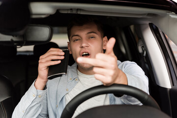 drunk man holding flask with alcohol and showing middle finger in car, blurred foreground.