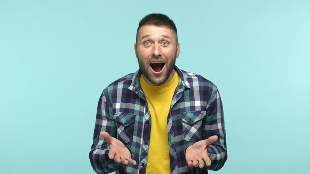 Slow motion of handsome young man feeling happy for you, raising eyebrows hear surprising news and pointing hands at camera, congratulating, standing over blue background