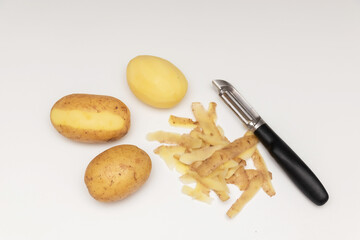 Fototapeta na wymiar Raw peeled potatoes with a potato peeler on a white table, potato peel.
