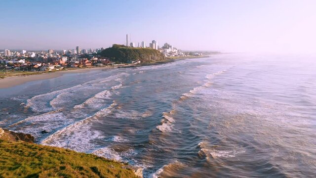 Aerial view from high grass rocky cliffs by atlantic ocean beach and city skyline on the back, Torres City, Rio Grande do Sul, Brazil