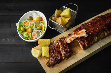 Barbecue ribs and potatoes on a wooden board. Coy space.