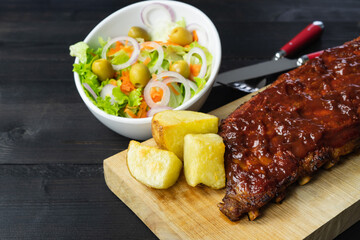 Barbecue ribs and potatoes on a wooden board.