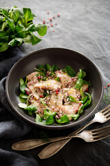 Herring salad with lamb's lettuce, chopped onion and herbs in a black bowl on a dark background 