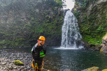 Fototapeta premium A vertical shot of a Hispanic cheerful rock climber in a helmet hat and safety harness showing a victory sign