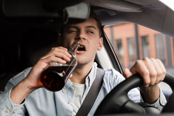 drunk man driving car and drinking whiskey on blurred foreground.